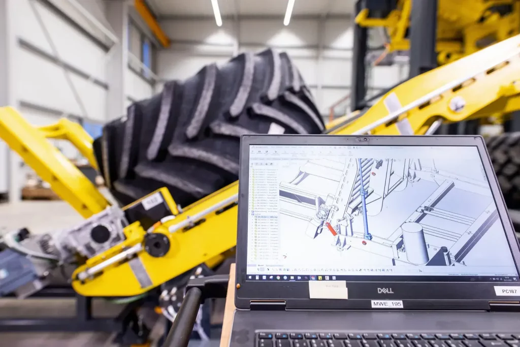 Foto der Konstruktion der Rädermontageanlage auf Laptop mit aufgebauter Maschine im Hintergrund